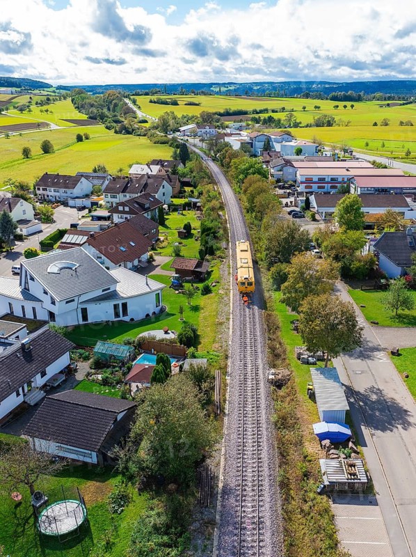 Aerial view of a village with railway line, surrounded by green fields and various houses, tamping machine, Hermann Hessebahn, Althengstett, Black Forest, Germany