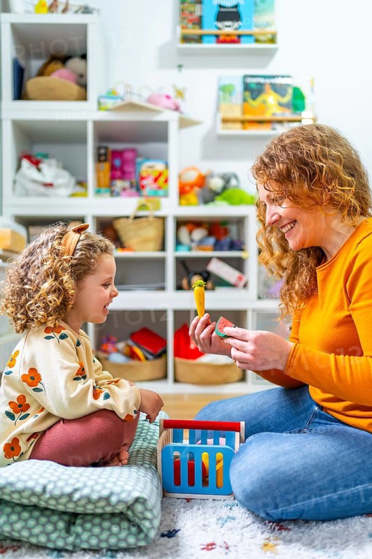 Vertical photo of a cute girl and mother playing with toys in the bedroom together