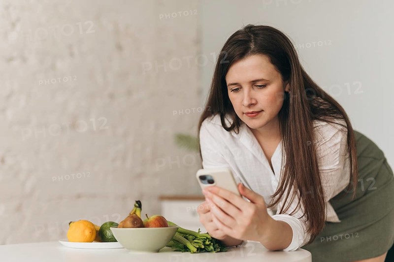 Nutritionist examines smartphone while leaning on table with fresh fruits and vegetables. Concept of healthy eating, balanced diet advice, and lifestyle management