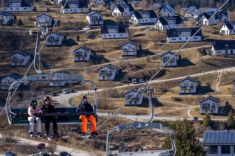 Winter sports area in the Sauerland, Winterberg ski lift carousel, artificial snow slopes, artificial snow from over 360 snow guns, Büre-Herrloh ski area, 12 of 24 lifts are in operation in mid-March, the rest of the landscape is snow-free, in the background holiday homes at Landal Ferienpark Winterberg, North Rhine-Westphalia, Germany