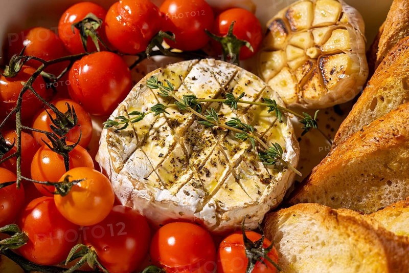 A delicious baked Camembert cheese accompanied by fresh cherry tomatoes, roasted garlic, and crispy bread slices. Perfect for a gourmet appetizer or snack