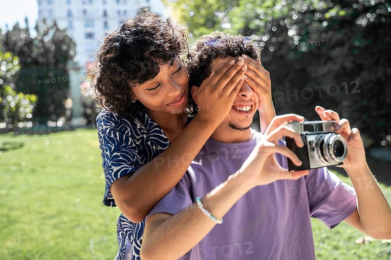 A joyful multiethnic LGBTQ+ couple shares a playful moment in a sunlit park, enjoying each other's company and the beauty of the day