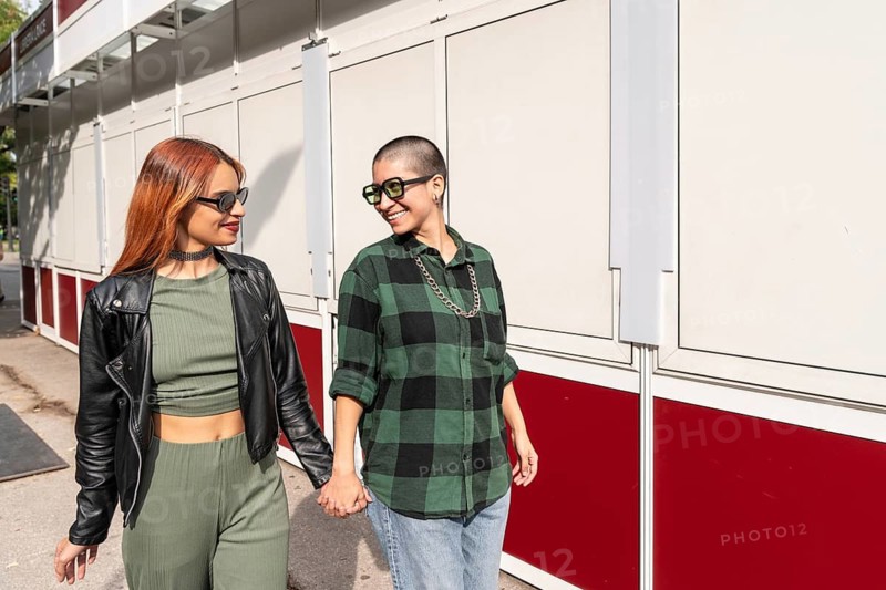 A Colombian lesbian couple holds hands, walking side by side, sharing a joyful moment while embodying love, diversity, and acceptance in an urban setting