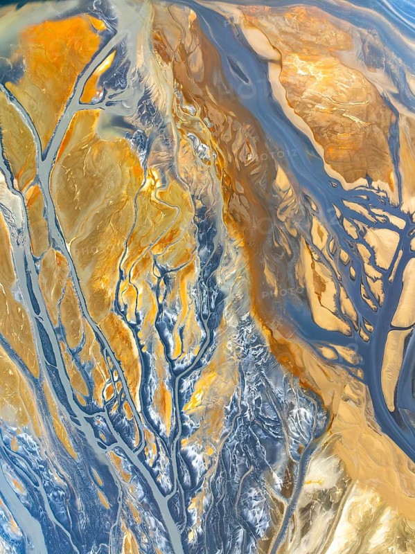 Top view captured by a drone, showcasing a mesmerizing abstract pattern of nature textures, with intertwining blue and gold hues with rivers in the landscapes