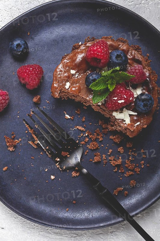 Half-eaten chocolate tartlet, on a plate, stuffed with cottage cheese and berries, breakfast, homemade, no people
