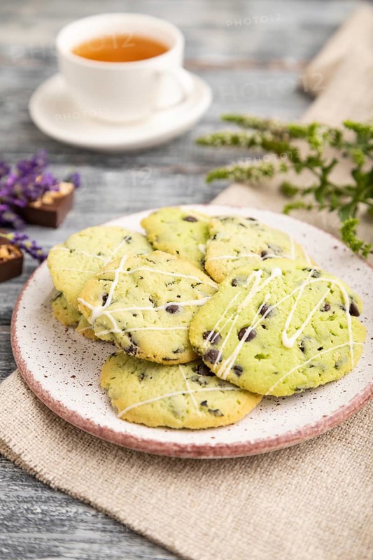 Green cookies with chocolate and mint on ceramic plate with cup of green tea and linen textile on gray wooden background. side view, close up, selective focus