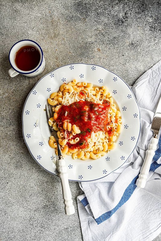 A delicious serving of chifferi rigati pasta topped with rich tomato sauce and grated cheese on a white plate. A perfect meal for Italian cuisine enthusiasts