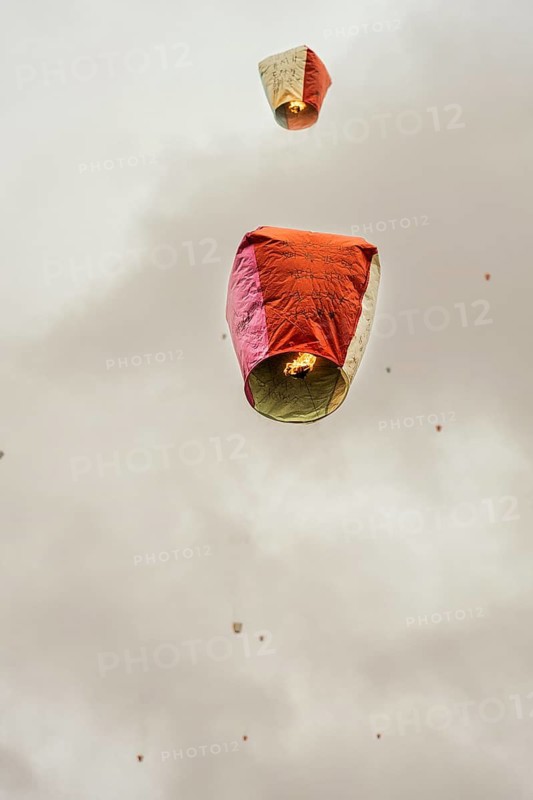 Low angle view of traditional red and cream Chinese floating lanterns in the sky, as seen in Taiwan. These lanterns, typically used during festivals, are adorned with blessings and wishes for health, happiness, and prosperity