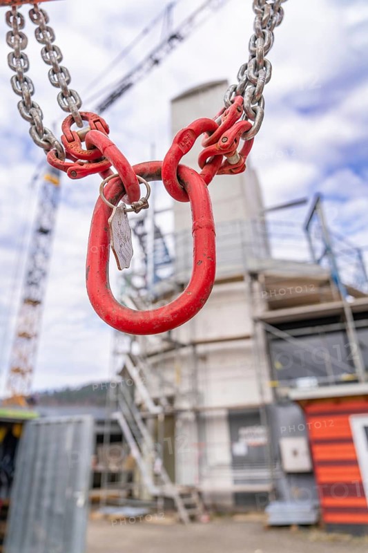 Large red hook with chain hangs in front of a blurred construction site background, staircase extension to the new tower of the Calw railway station on the new track of the Hermann Hessebahn, Calw, Black Forest, Germany