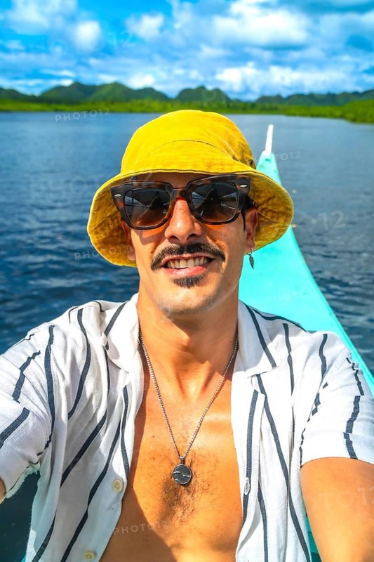 Young man wearing sunglasses and bucket hat taking selfie while enjoying boat trip in the beautiful turquoise waters of siargao island, philippines