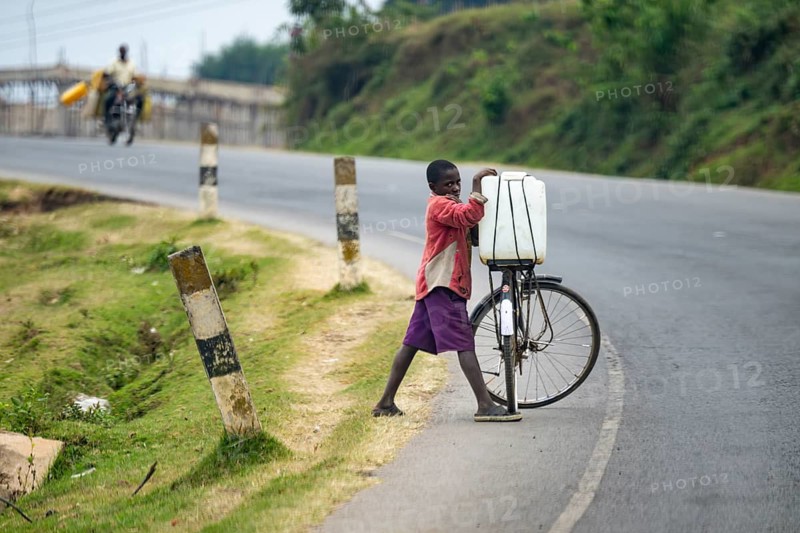A boy transports water on a bicycle on a country road, street scene in rural Uganda, western region, Uganda