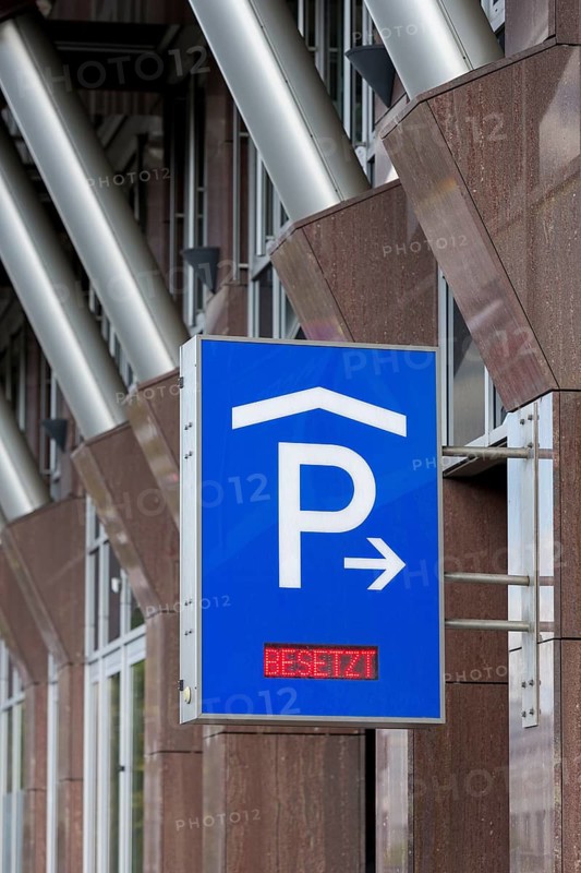 Blue car park sign with white P symbol and red display with the words 'Occupied' in front of modern architecture, Baden-Württemberg, Germany