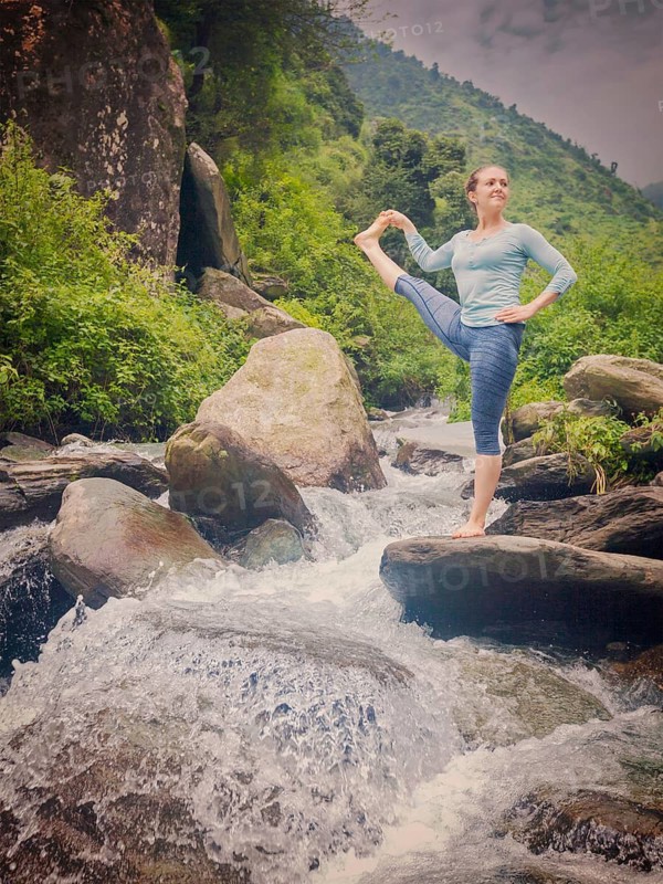 Yoga outdoors, woman doing Ashtanga Vinyasa Yoga balance asana Utthita Hasta Padangushthasana, Extended Hand-To-Big-Toe Pose position posture outdoors at waterfall. Vintage retro effect filtered hipster style image