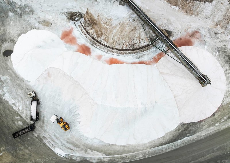 Salt heaps with conveyor belt, lorry and excavator at the salt works of Walvis Bay Salt. Aerial view. Drone shot. Walvis Bay, Namibia