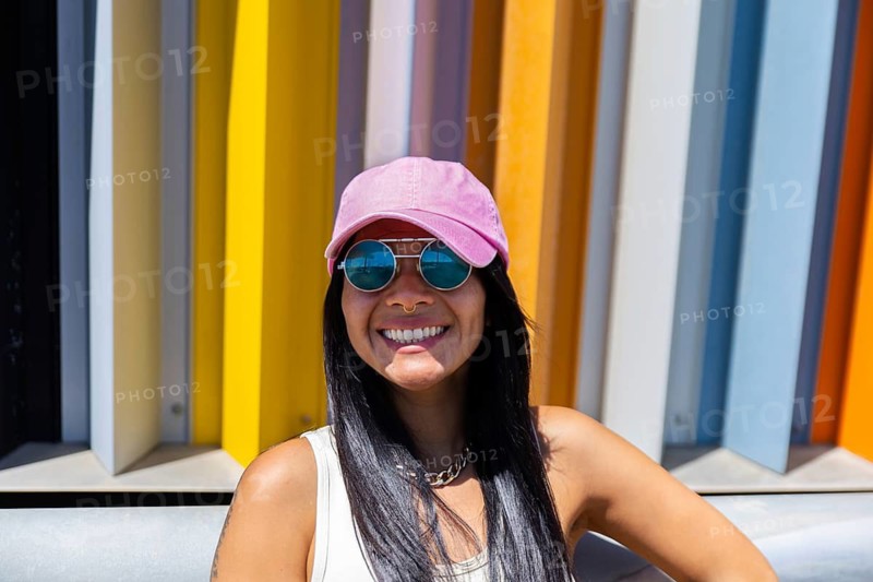 A woman in a vibrant outfit stands confidently against a backdrop of colorful, modern architecture. Her attire contrasts with the urban environment, creating a striking visual effect