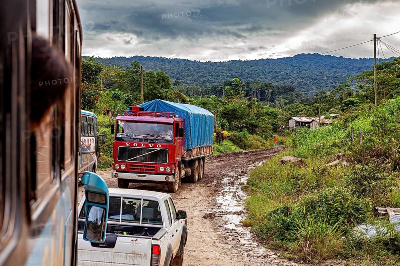 A truck and a pickup truck on a muddy country road surrounded by dense nature, traffic on Yungas road in the rainforest of Bolivia