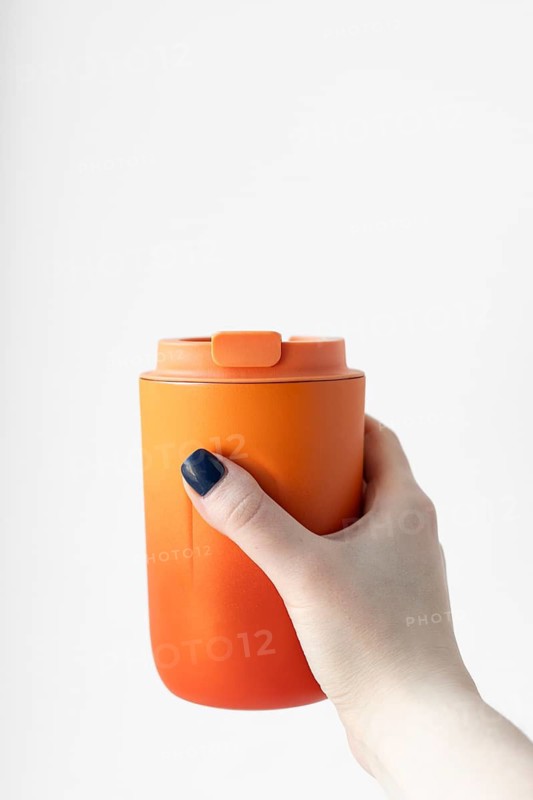 Cropped unrecognizable woman holding an orange thermo cup, highlighting an eco-friendly concept with a simple, clean background