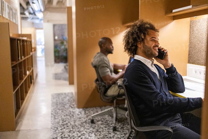 Two professionals engaged in work at a coworking space in Barcelona. One person is smiling on the phone, while another works on a laptop, creating a productive atmosphere