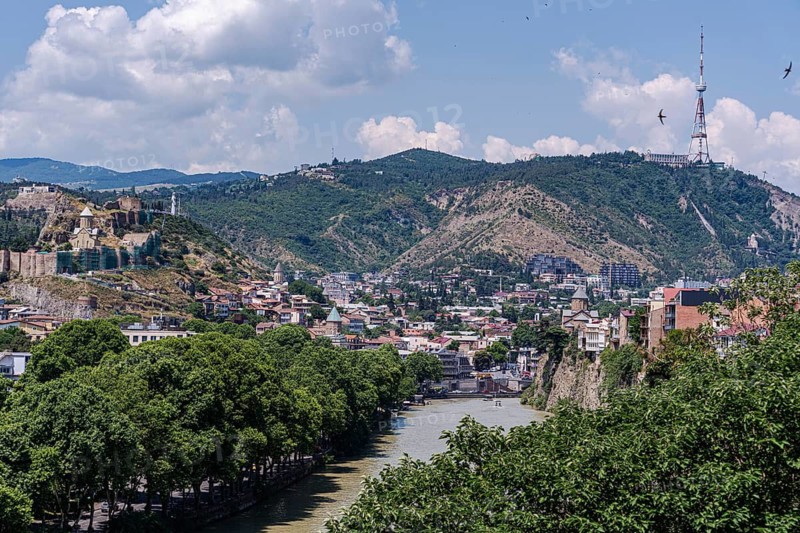 A breathtaking view of Tbilisi showcasing the scenic beauty of its lush green hills, historic architecture, and the winding Kura River under a vibrant blue sky