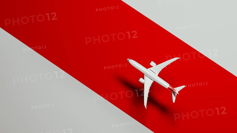 From above a sleek commercial airplane soars gracefully above a vivid red background, symbolizing travel and adventure in the skies