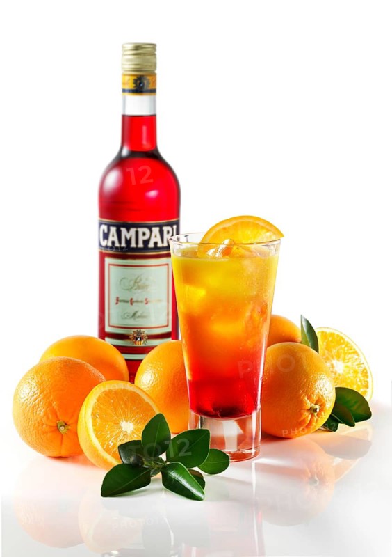 Cocktail Campari Orange on ice cube cubes in a long drink glass in front of a white background, half an orange slice as garnish, oranges and orange leaves as bottom decoration, Campari bottle behind, studio shot
