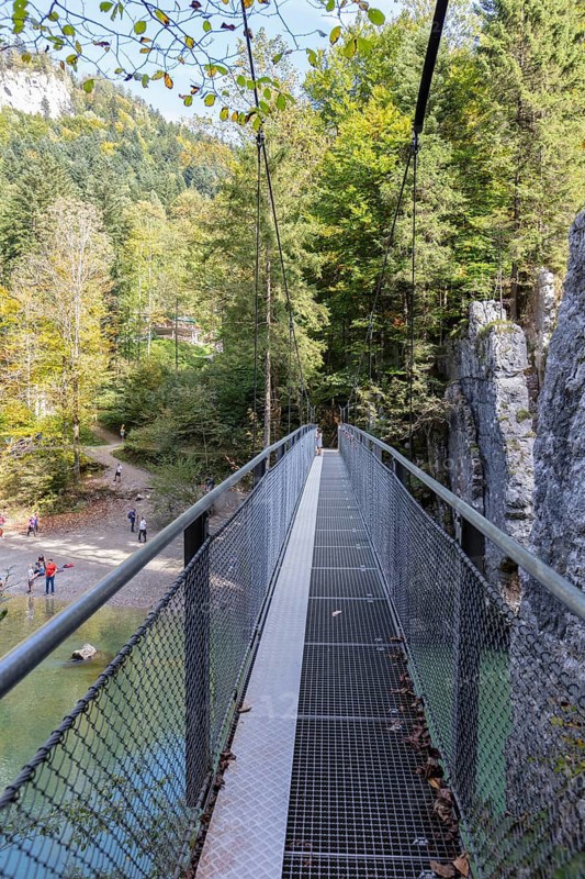 A long suspension bridge that leads through a rocky forest path, surrounded by nature, Klobenstein