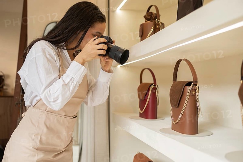 A photographer takes detailed shots of elegant handbags on display in a boutique store. Various leather handbags with chic designs and chain straps are showcased on shelves
