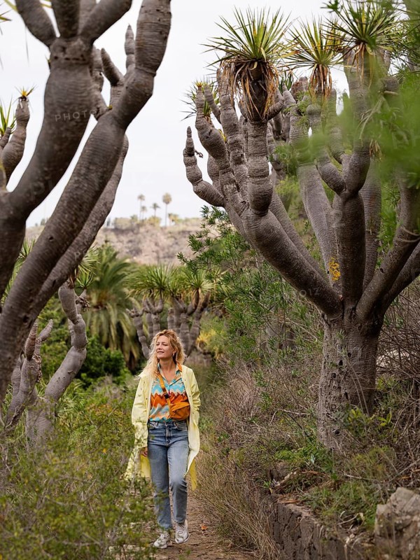 A woman enjoys a serene walk amidst the towering dragon trees and lush greenery of Viera y Clavijo Botanical Garden in Las Palmas, Gran Canaria
