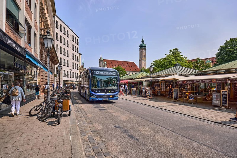 Public transport, public transport, bicycles, shopping market, fixed and mobile market stands, advertising displays, general architecture, commercial buildings, façade with windows, awnings, shops, shopping, church tower of the Holy Spirit, trees, pedestrians and market visitors as secondary motifs, image processing contrasts, pale blue sky, cumulus clouds, cirrostratus clouds, slightly diffused and sunny light, victuals Market, Munich, state capital, independent city, Bavaria, Germany