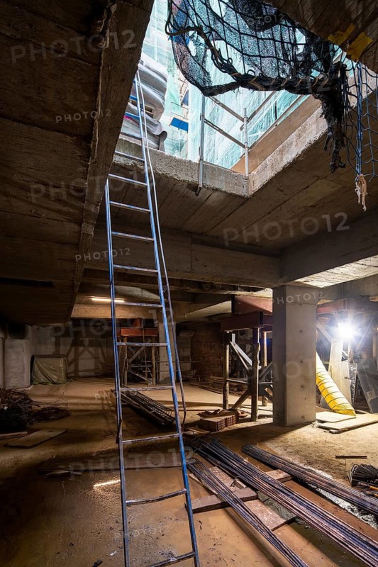An indoor construction site with essential elements like ladders, pillars, and building materials, highlighting progress. Dim lighting emphasizes an unfinished yet promising state