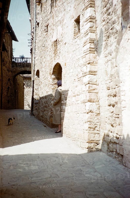 A tourist tries to make friends with a cat in an Italian village alley, Italy, 1957