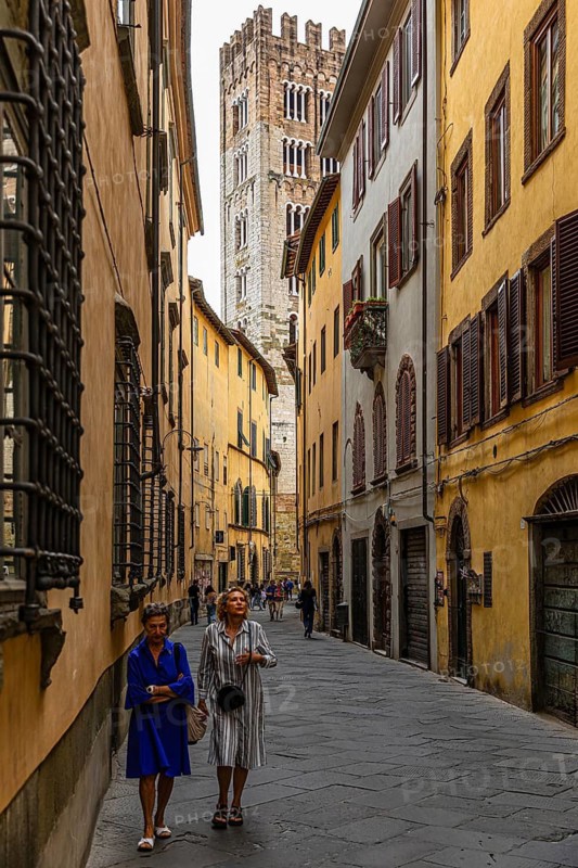 Two ladies walking through a narrow alley, behind them the tower of San Martino Cathedral, historic city centre, Lucca, Tuscany, Italy