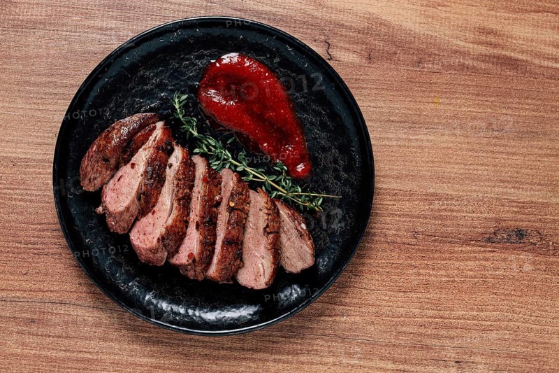 Roast duck breast, sliced on a plate, with red sauce, homemade, no people