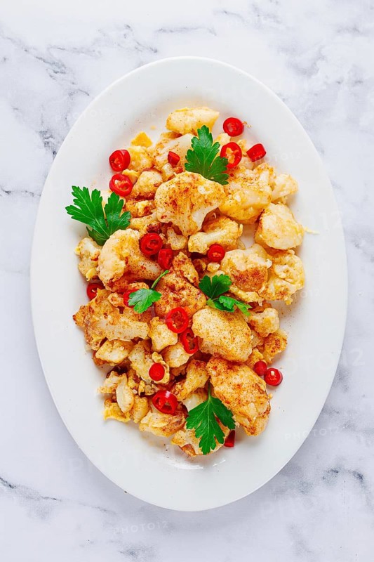 Cauliflower dish, with chili pepper and parsley, on a white plate served on a marble countertop