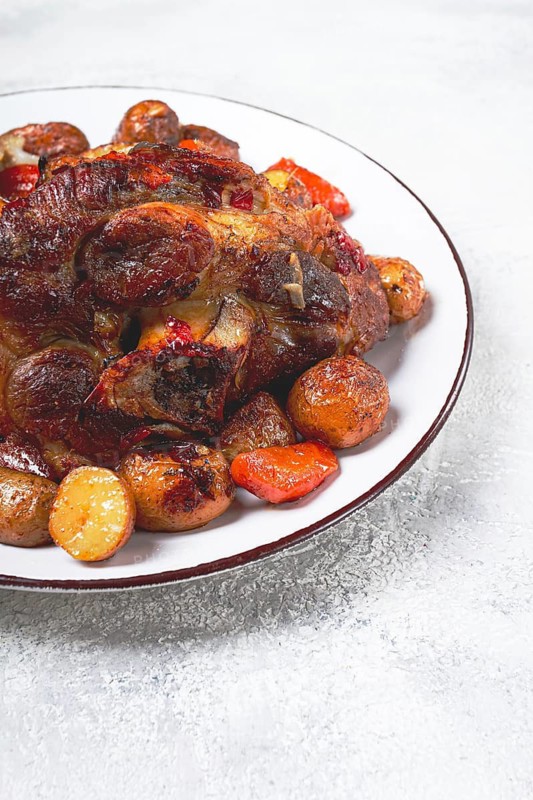 Pork knuckle baked with vegetables, new potatoes, on a white plate, homemade, no people