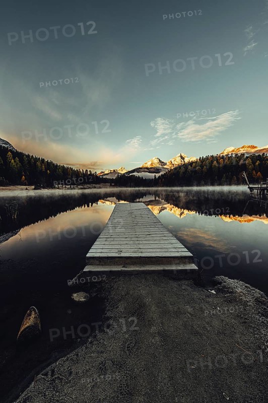 Lake Staz near Sankt Moritz in the Engadin in Switzerland. Morning atmosphere with fog in autumn. Water reflection and snow-covered mountains in the background