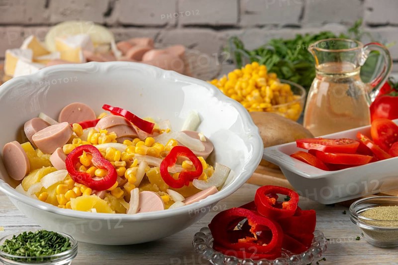 Colourful mix of potatoes, peppers, sausage and corn in a bowl surrounded by other salad ingredients
