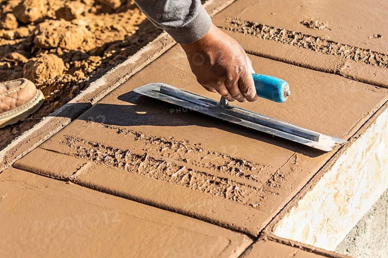 Construction Worker Using Trowel On Wet Cement Forming Coping Around New Pool