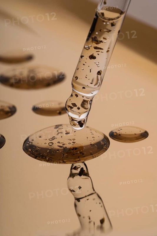 Close-up image of a pipette dispensing anti-aging face serum enriched with golden particles, accentuating the product's luxury and skin benefits
