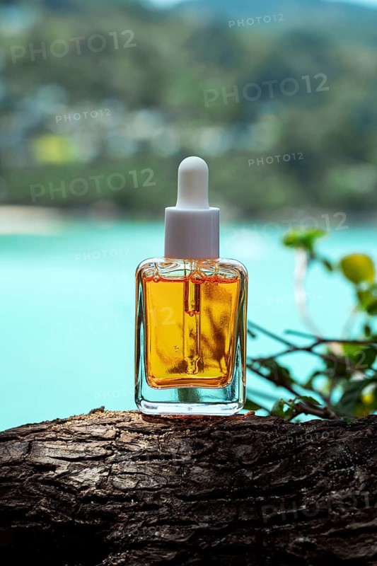 Golden cosmetic serum enriched with vitamins displayed on a tree trunk by a turquoise sea, highlighting the luxury of natural skincare ingredients