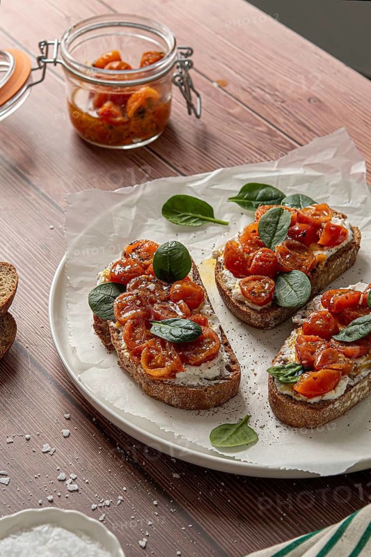Rustic bruschetta topped with creamy cheese, marinated cherry tomatoes, and fresh spinach. Served on a wooden table, offering a delicious mix of flavors and textures