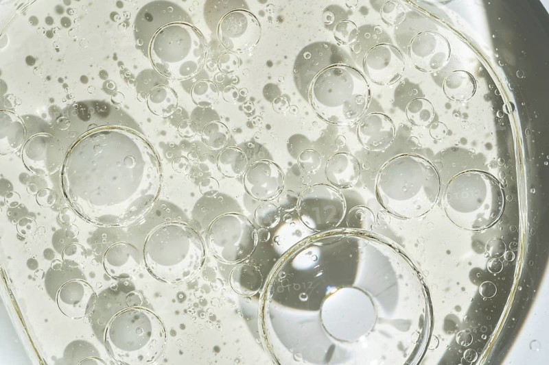 A detailed macro shot of transparent oil bubbles on a shiny surface. The intricate patterns of bubbles create an abstract and scientific visual impression