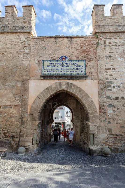 Old city gate with stone walls and a passage through which people walk, Tarifa