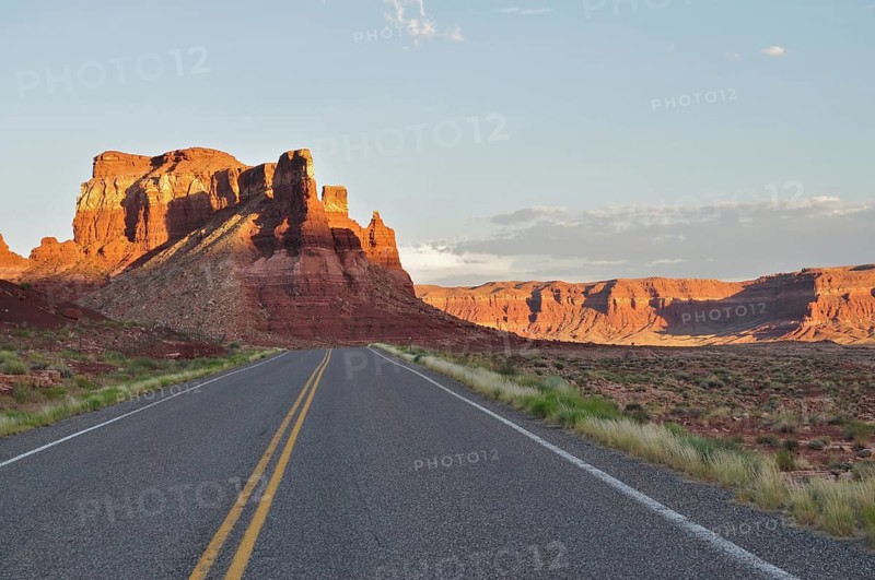 An open road leads through a red rock landscape in the warm light of sunset, Lake Powell, Arizona, USA