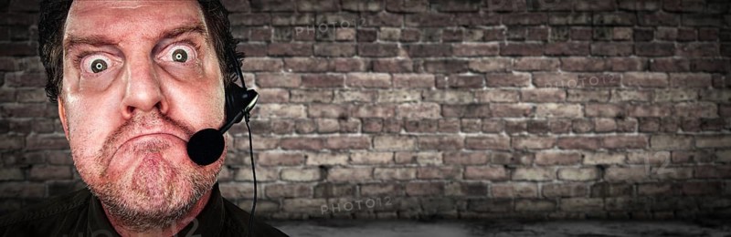 Grumpy Businessman with Frowning Face Wearing Phone Headset In Office with Brick Background Banner