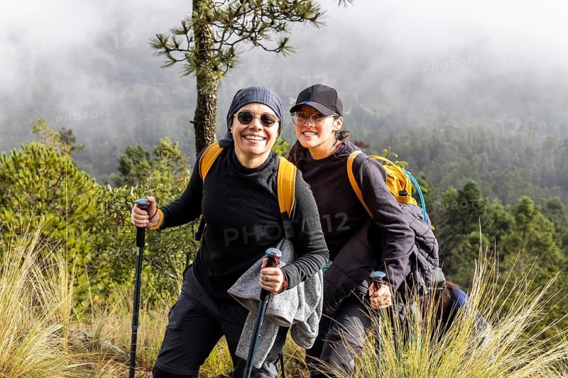A cheerful pair of hikers smiles while trekking through a misty forest. Equipped with backpacks and walking sticks, they embrace the adventure and scenic views around them