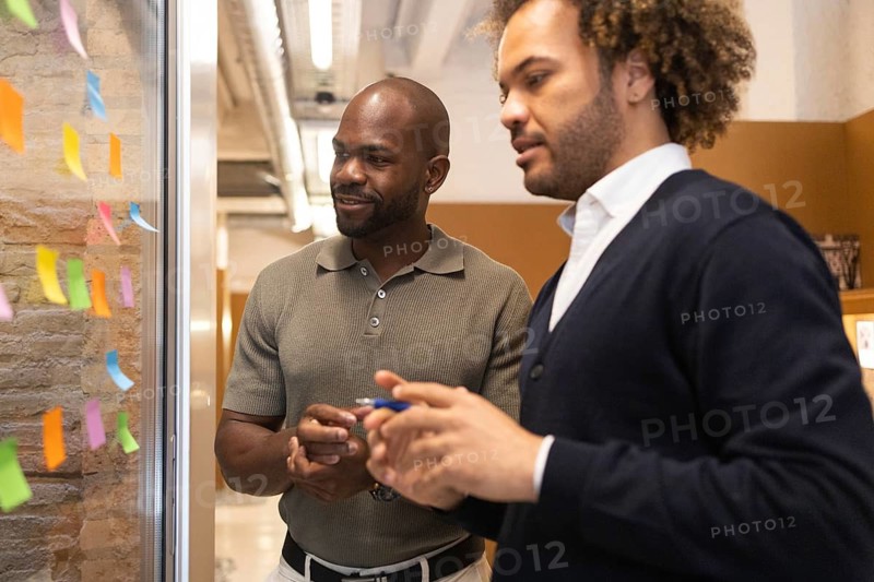 Two professionals engage in brainstorming at a coworking space in Barcelona. They discuss ideas, using colorful sticky notes as tools for creative planning and strategy development