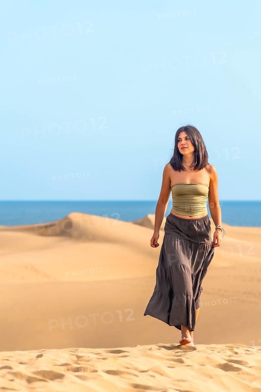 Young woman enjoying walking barefoot on the sand dunes of maspalomas with the ocean in the background