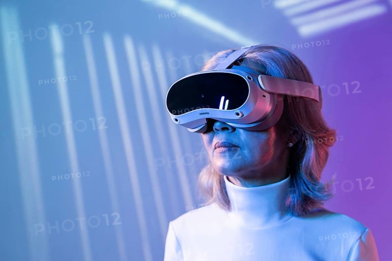 An elderly Asian woman wearing virtual reality goggles immerses herself in the metaverse. The image reflects the diversity of users engaging with advanced digital technologies