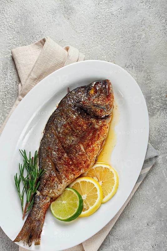 Baked dorado fish, in the oven, fried dorado, with spices and herbs, on a white plate, top view, homemade, no people